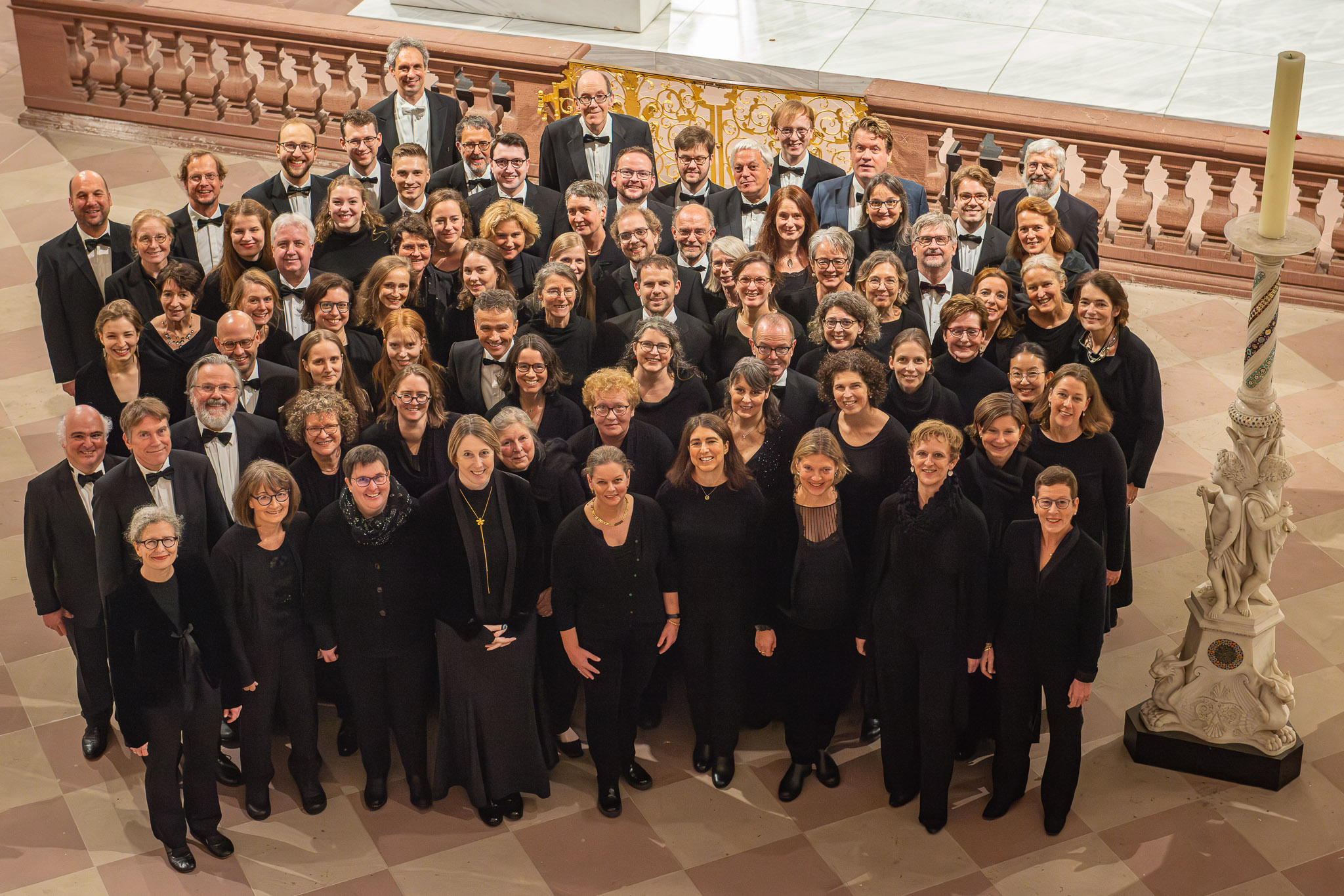 großer gemischter Chor, schwarz gekleidet, in einer Kirche, alle schauen freundlich nach oben