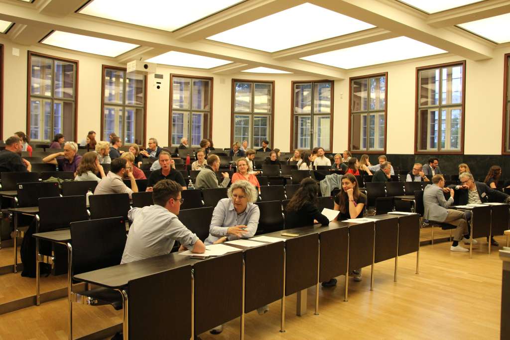 Teilnehmende in einem Hörsaal im Gespräch mit Nachbarn