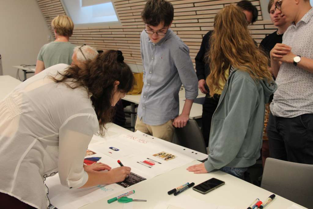 junge Studierende im Gespräch, gestalten Plakat auf einem weißen Tisch