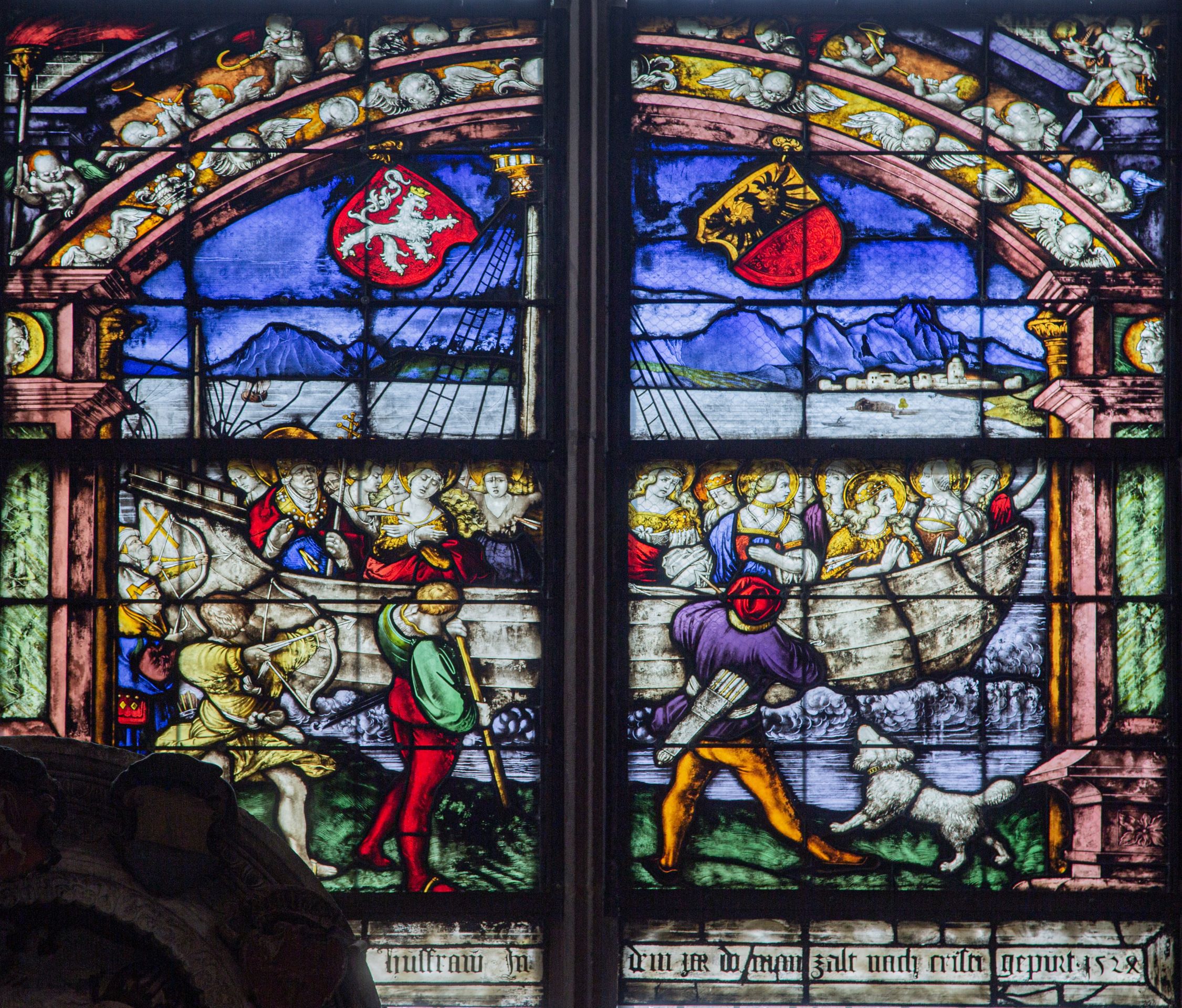 buntes Kirchenfenster, viergeteilt, oben strahlend blau mit 2 Wappen, unten ein Schiff voller Frauen mit Heiligenschein (Legende der Heiligen Ursula)