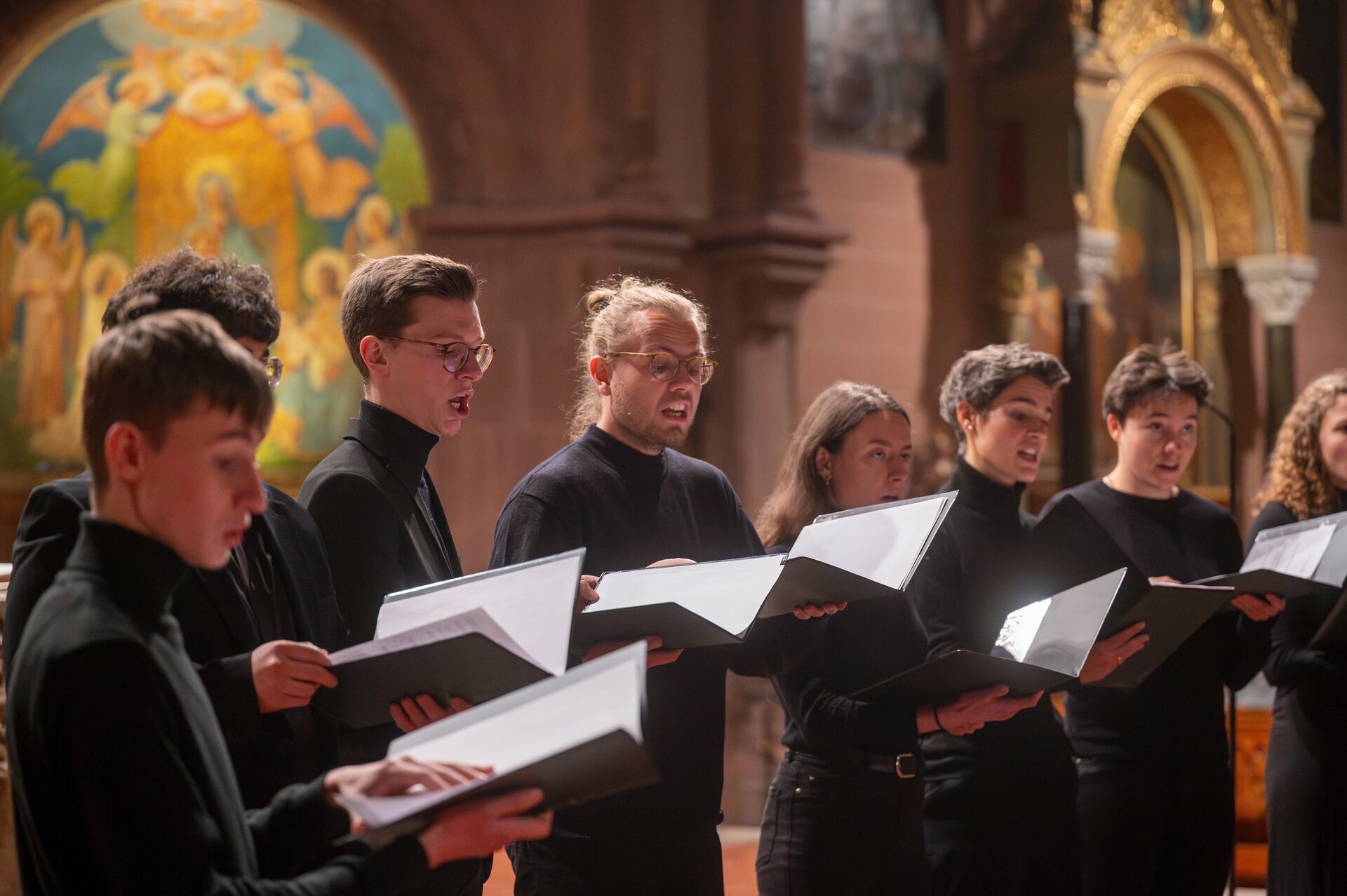 8 Sänger und Sängerinnen, schwarz gekleidet, Notenmappen in den Händen in einer Kirche