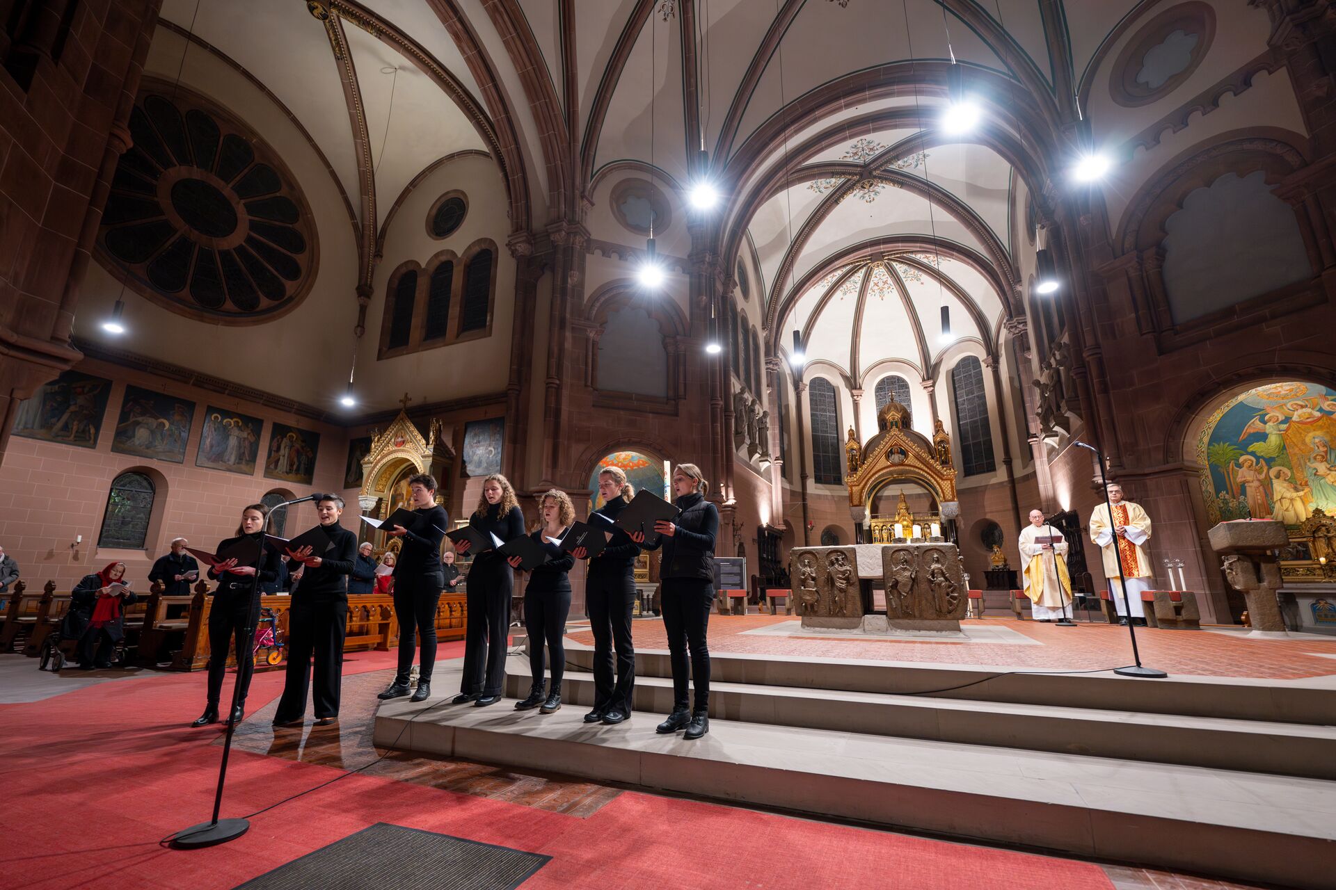 7 Sänger und Sängerinnen stehen nebeneinander vor dem Altarraum einer großen Kirche in einem Gottesdienst
