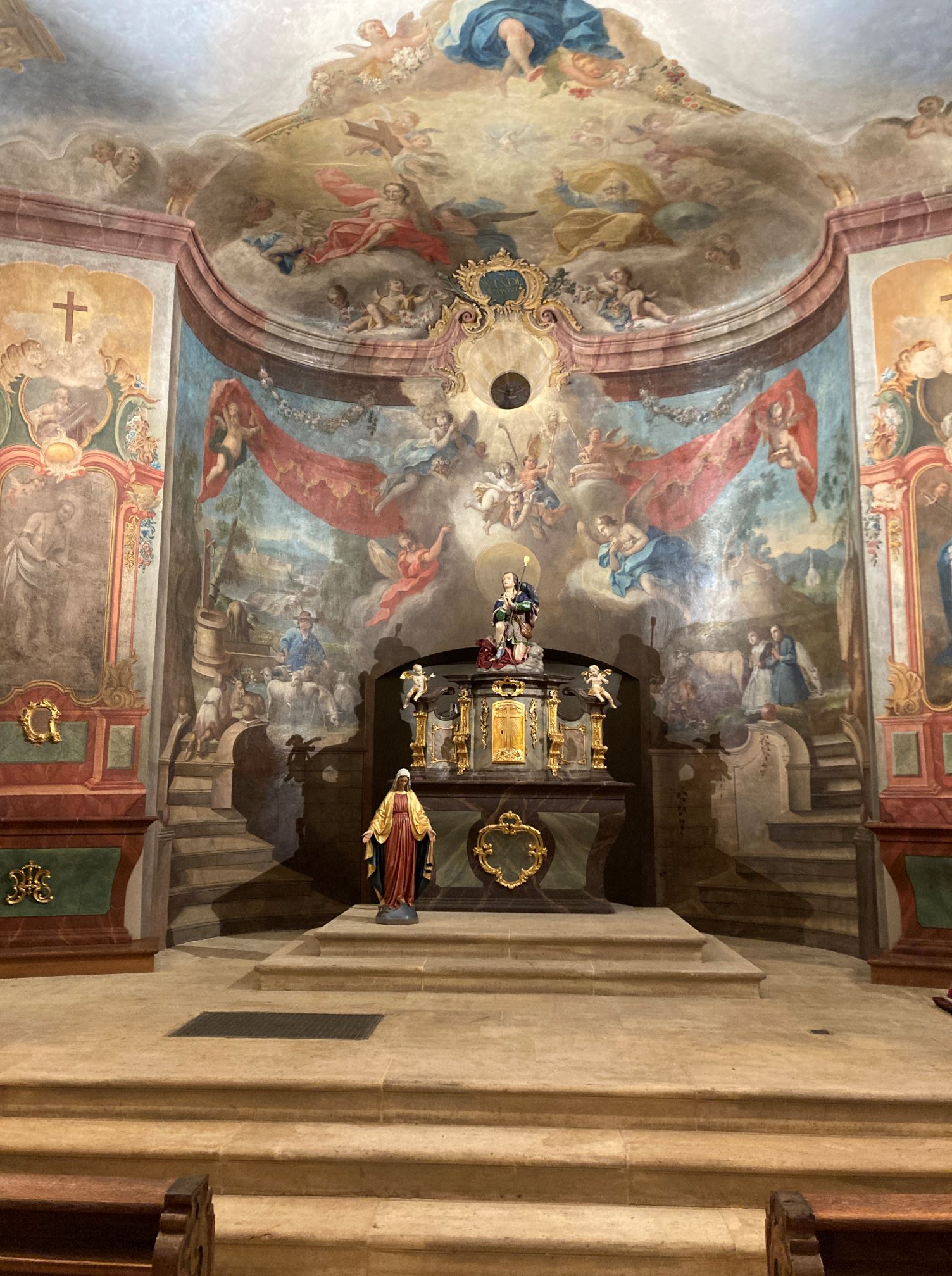 Blick in den barocken Chorraum einer Kirche mit Wandgemälde bis an die Decke und Deckengemälde, Blick in den Himmel mit vielen Engeln