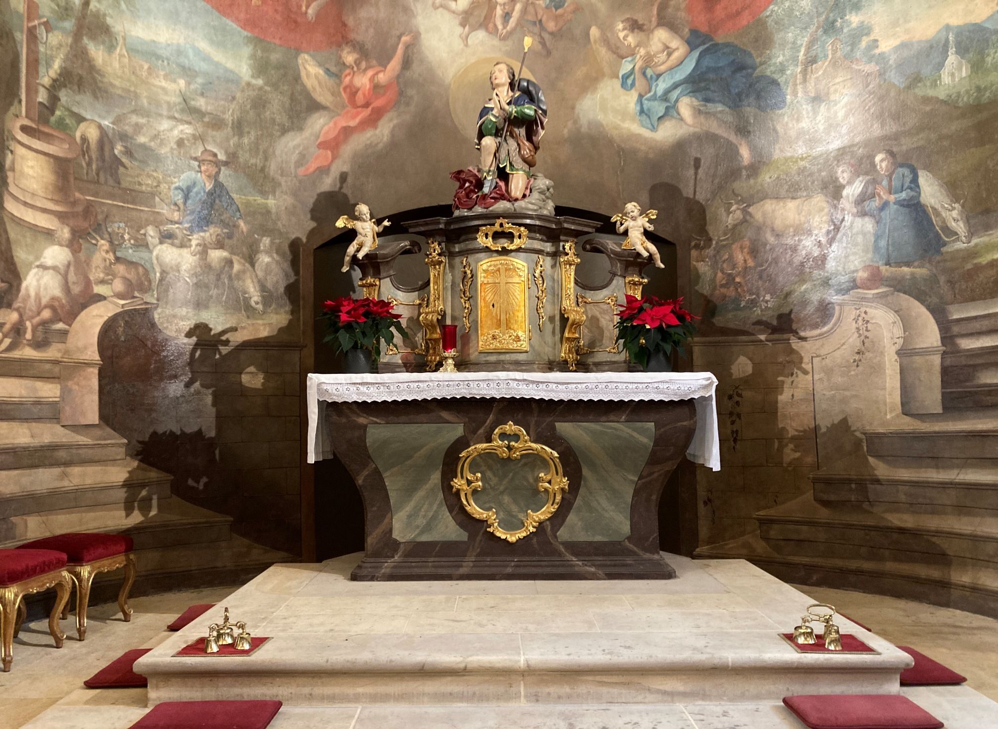barocker Altar in braun, grün und gold mit Engeln und Heiligenfigur. Im Hintergrund ein Waldgemälde mit emporsteigenden Treppen und betenden Figuren und Engeln.