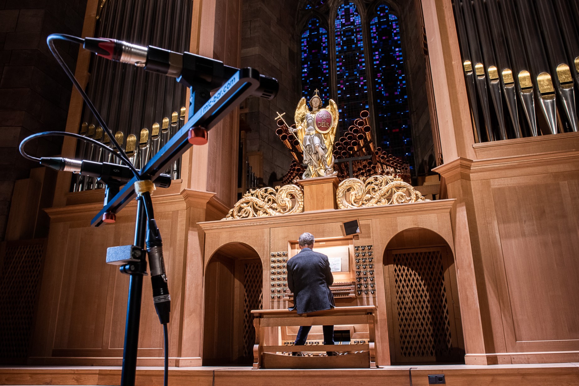 große Orgel mit der Figur eines großen Engels oben, dahinter blau leutendes Fenster, am Spieltisch der Organist von hinten, vorne ein Aufnahmegerät