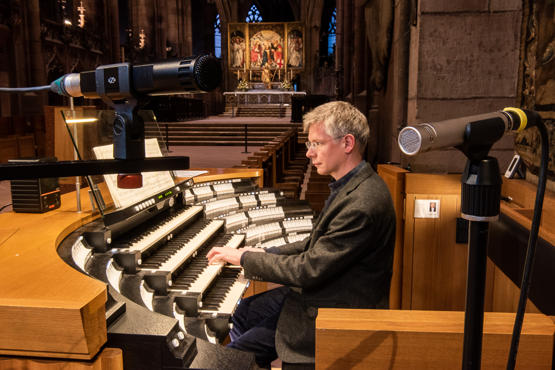 Organist am Spieltisch im Chor einer großen Kirche, vorne zwei Mikrofone
