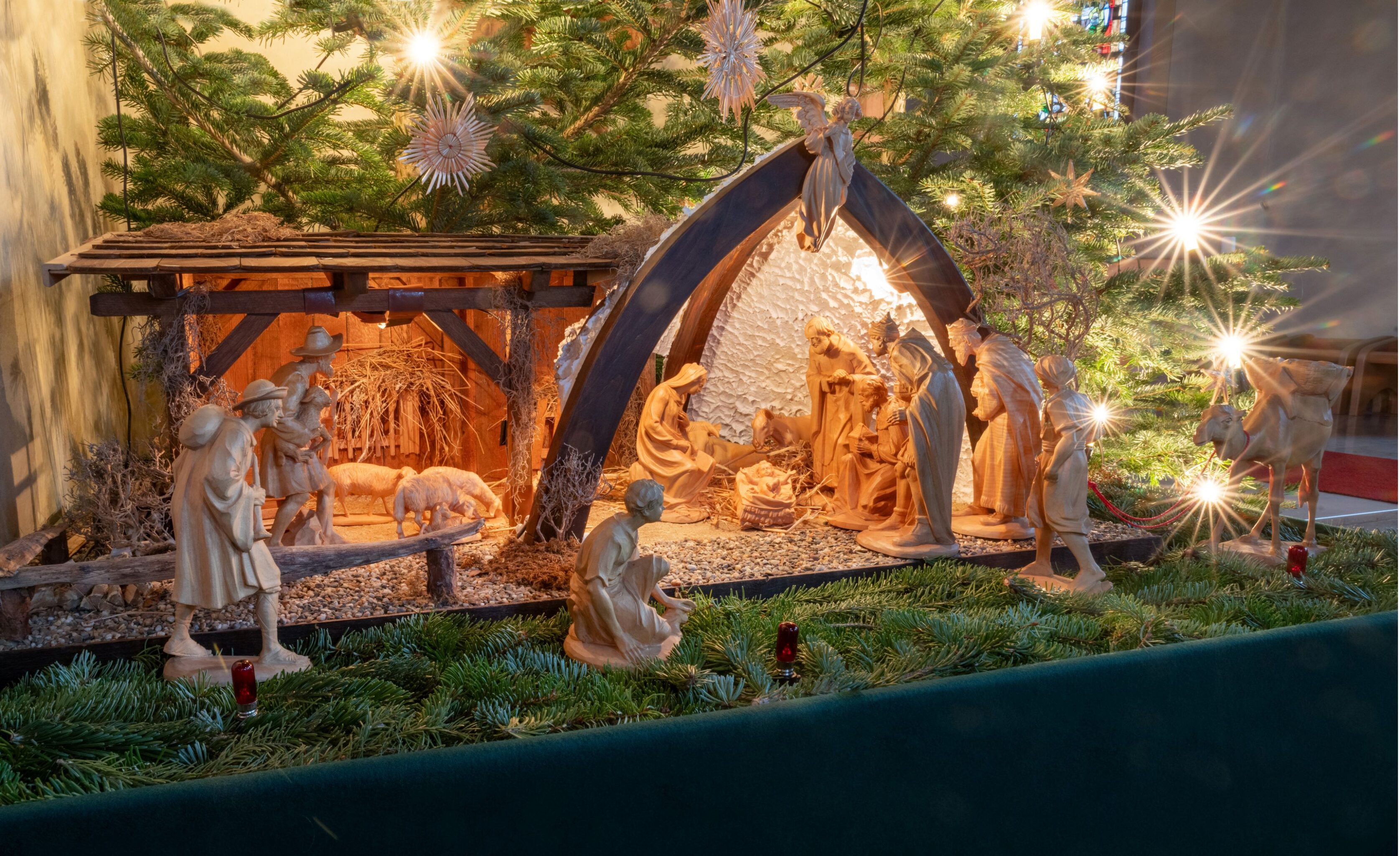 Krippe mit Holzfiguren unter einem Tannenbaum mit Strohsternen