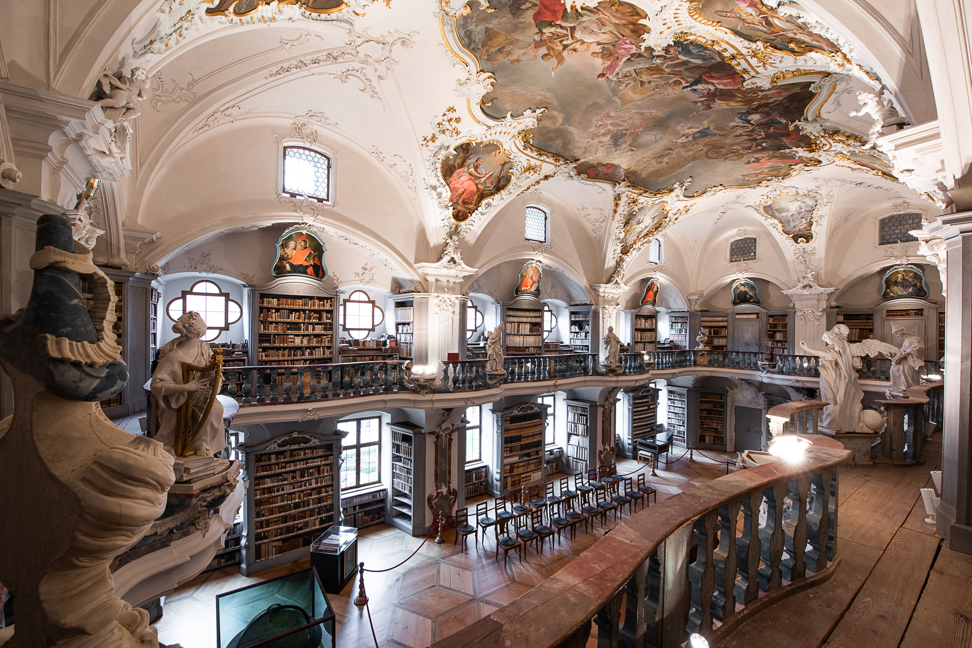helle, barocken Bibliothek, hohe Bücherregale zwischen Fenstern auf zwei Etagen, großes Deckengemälte, Stuckverzierungen
