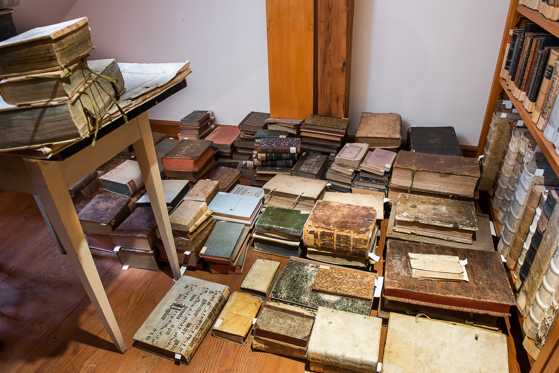 dicke, sehr alte Bücher liegen auf dem Boden, in Regalen und auf einem Tisch