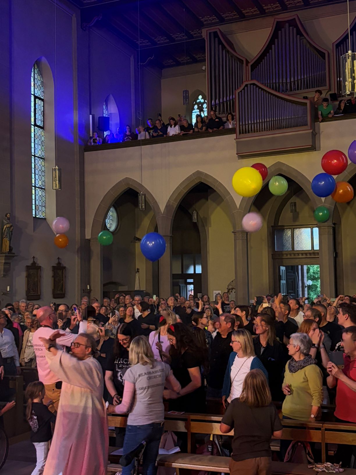fröhliche Menschen in einer Kirche, sie stoßen große bunte Luftballons in die Luft