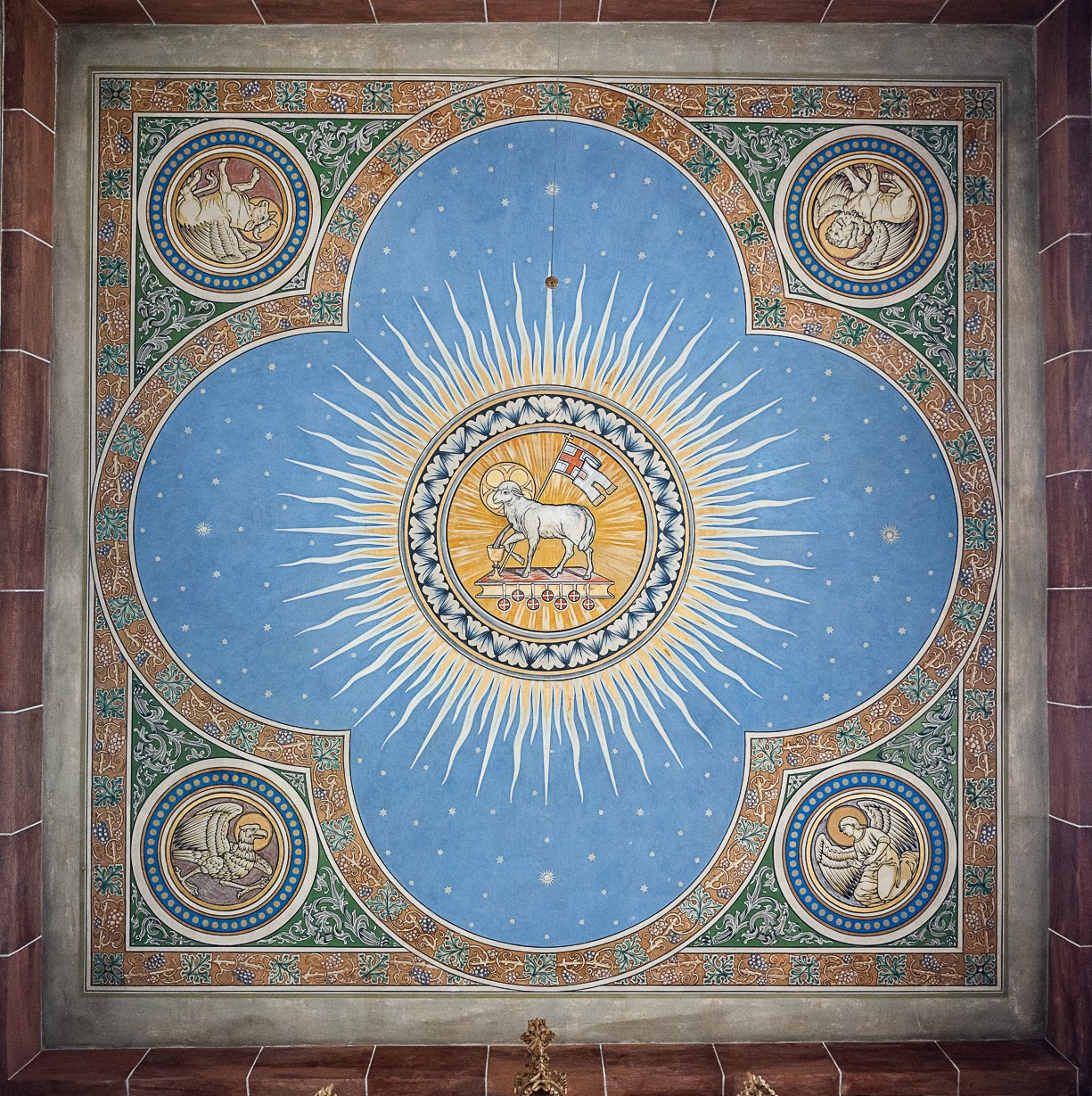 Deckengemälde in Kirche. Auf hellblauem Hintergrund in einem Strahlenkranz das Lamm Gottes, ein weißes Lamm mit Heiligenschein und einer Fahne vor einem goldenen Kelch