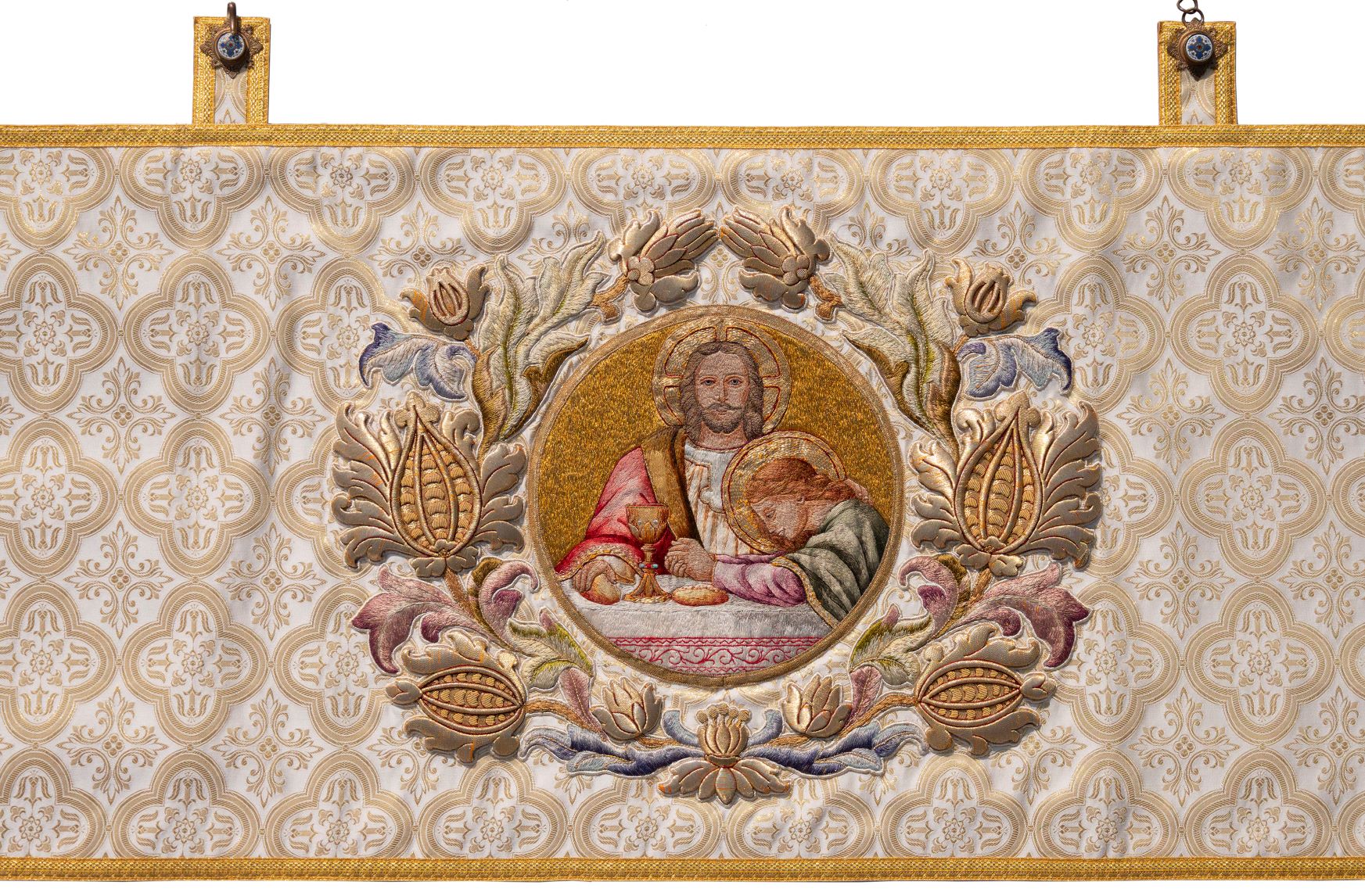 alter, bestickter Stoff, cremweiß mit goldenen Ornamenten, in der Mitte Jesus an einem Tisch mit Brot und Wein und neben ihm ein junge Frau, die sich mir gefalteten Händen über den Tisch beugt