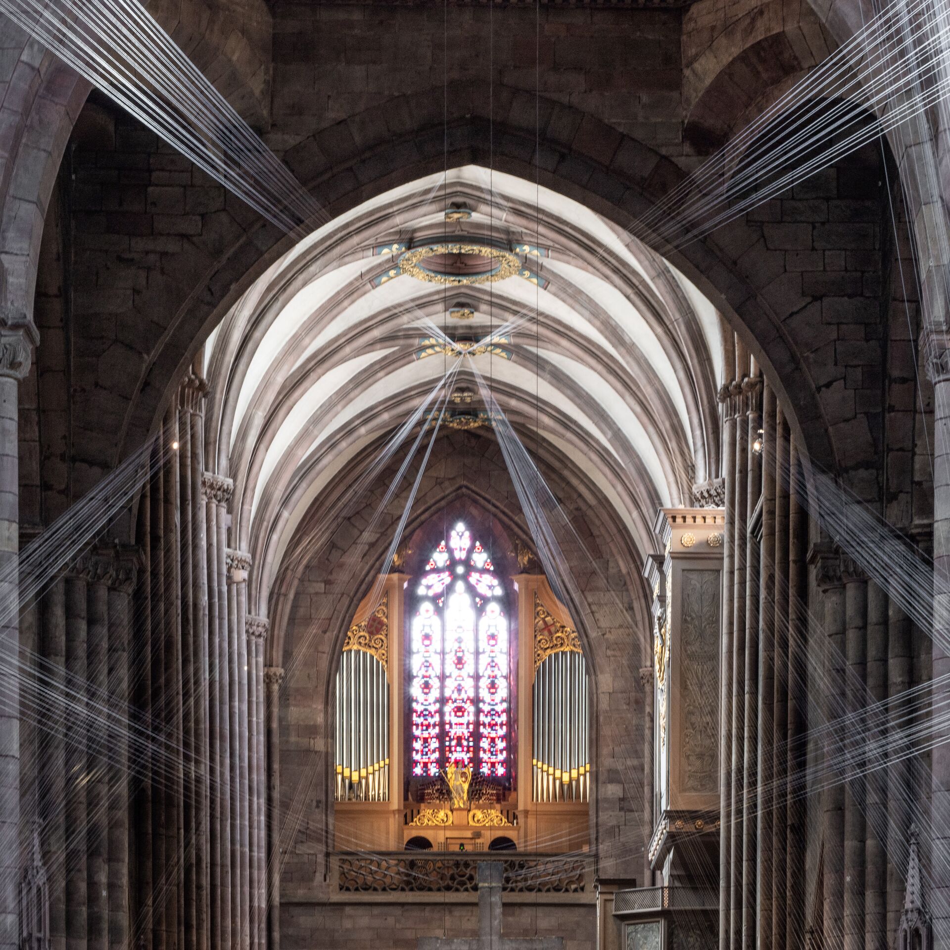 Blick durch das Langschiff einer gotischen Kirche nach hinten auf die Orgelempore. Fäden, wie aus LIcht, kommen auf den Betrachtenden zu.