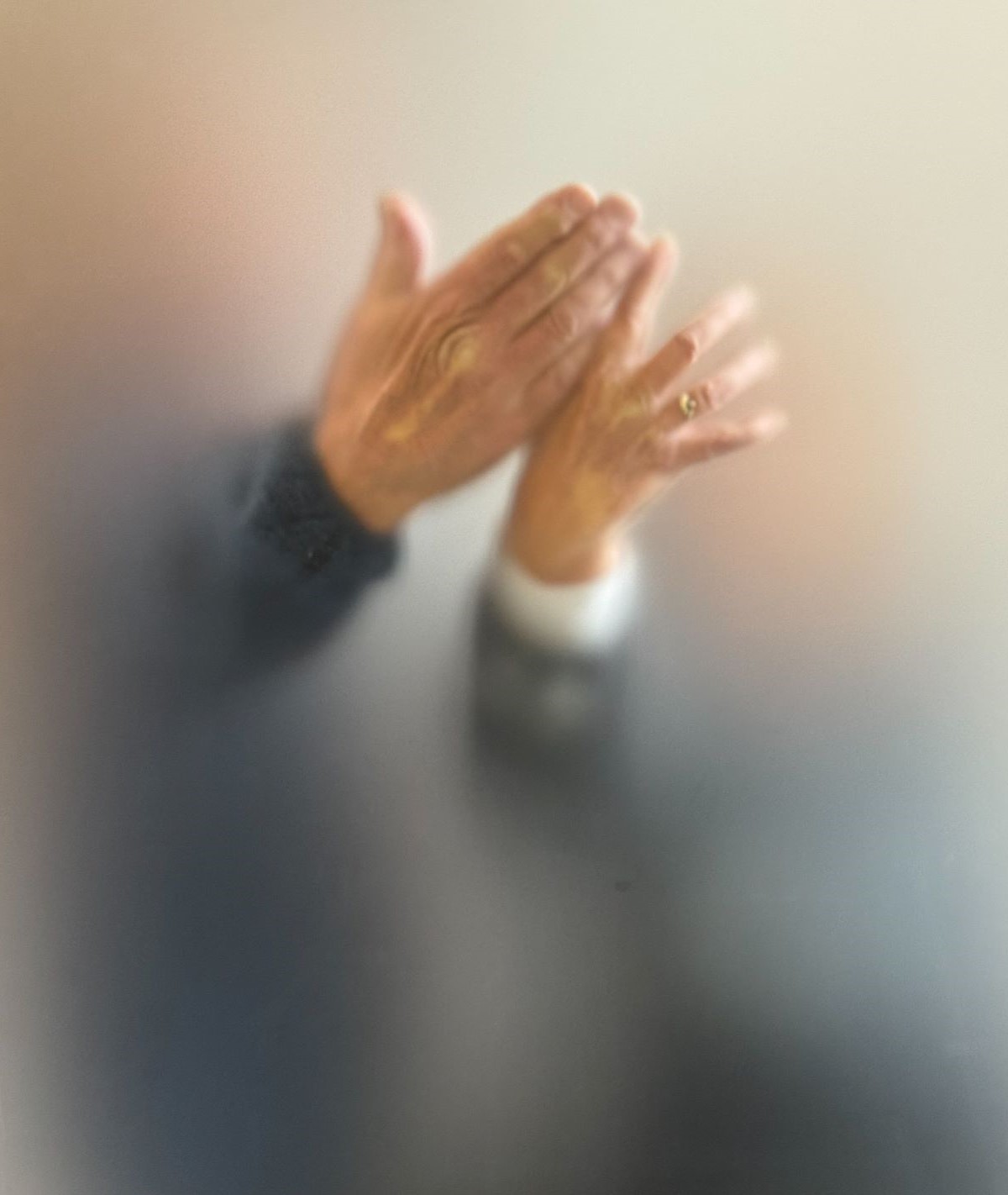 eine Männer- und eine Frauenhand, jeweils die Rückseite in inniger Berührung, Schemenhaft hinter einer Milchglasscheibe