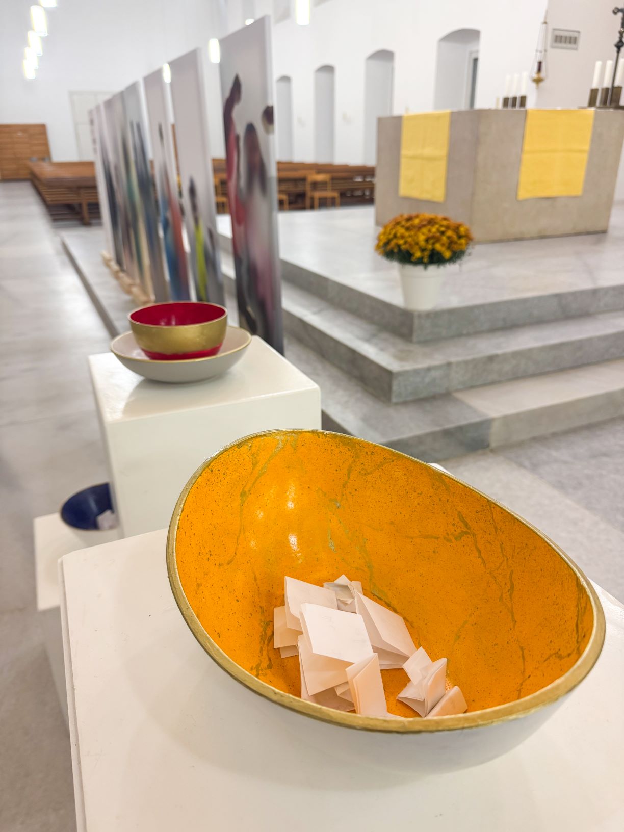 in einer Kirche eine gelbe Schüssel mit weißen, gefalteten Zetteln